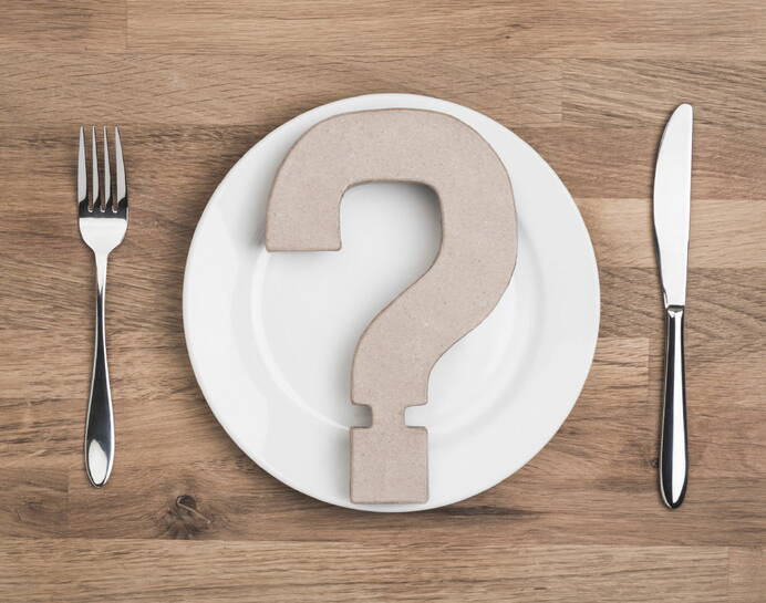 Teller mit Besteck auf einem Tisch. Im Teller liegt ein Fragezeichen aus Karton, das symbolisch für Fragen steht, wie man sich auf eine Magenspiegelung vorbereitet.